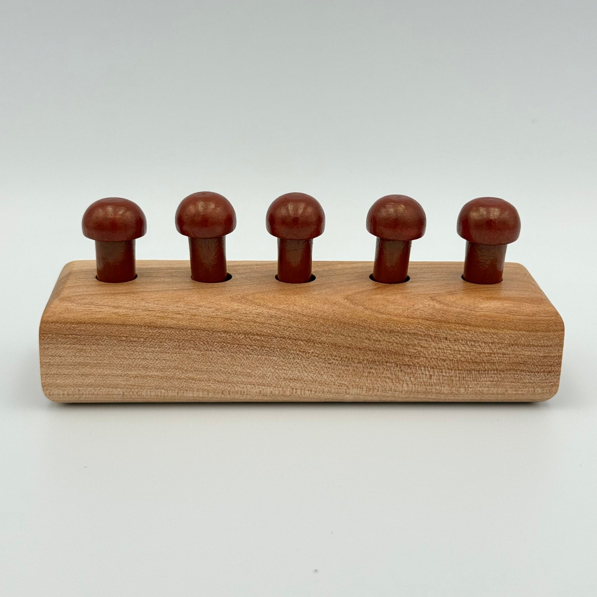 A wooden playing peg holder with dark rust color mushroom-shaped playing pieces, shown on a light gray background.