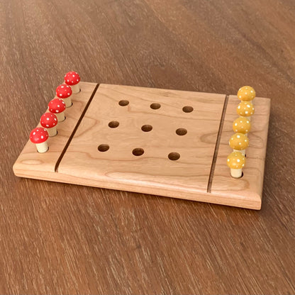 Solid cherry wood tic tac toe game board with red and yellow mushroom playing pegs sitting on a wooden surface