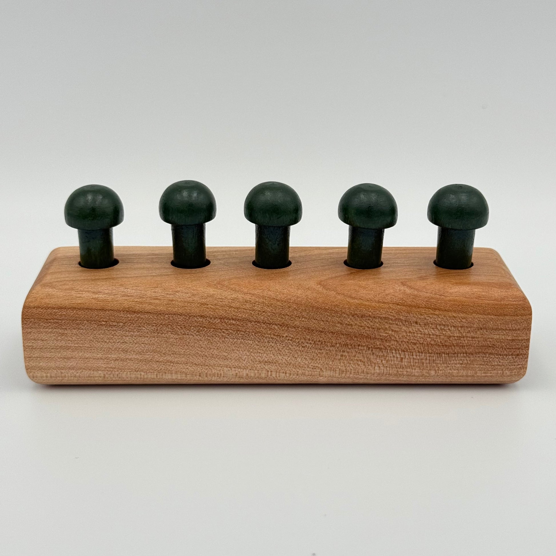 A wooden playing peg holder with dark green mushroom-shaped playing pieces, shown on a light gray background.