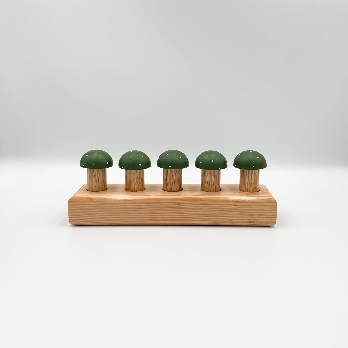 Green mushroom-shaped playing pegs sitting in a wooden block on a white background
