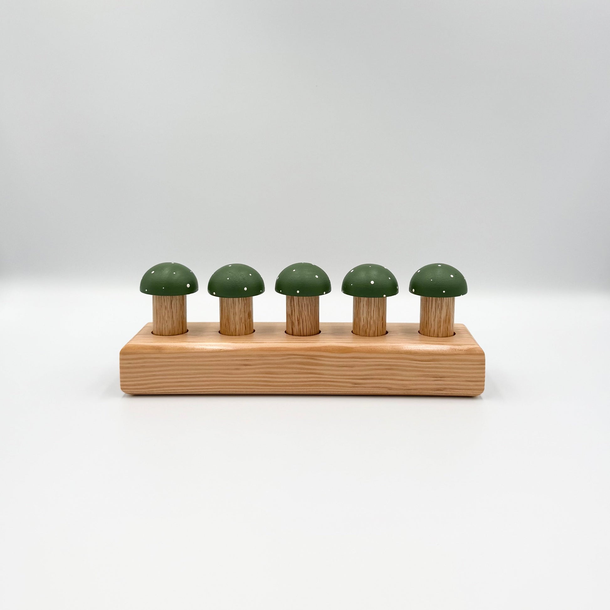 Green mushroom-shaped playing pegs sitting in a wooden block on a white background