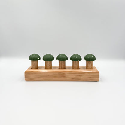 Green mushroom-shaped playing pegs sitting in a wooden block on a white background