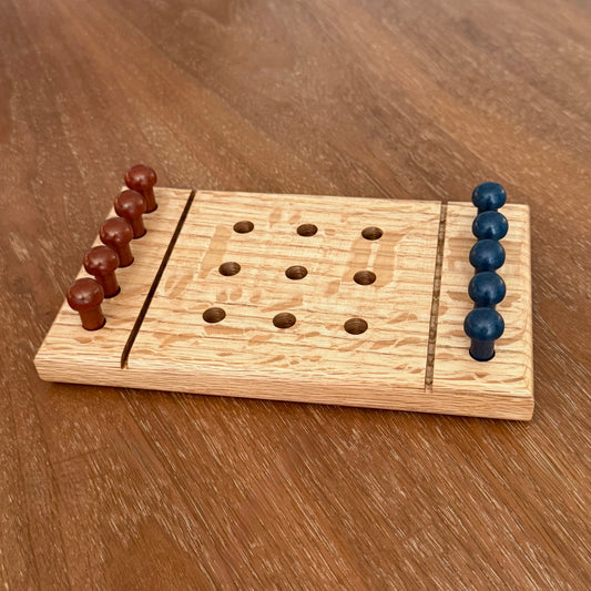 A small wooden tic-tac-toe game board  sitting on a table with rust colored playing pegs and dark blue colored playing pegs.