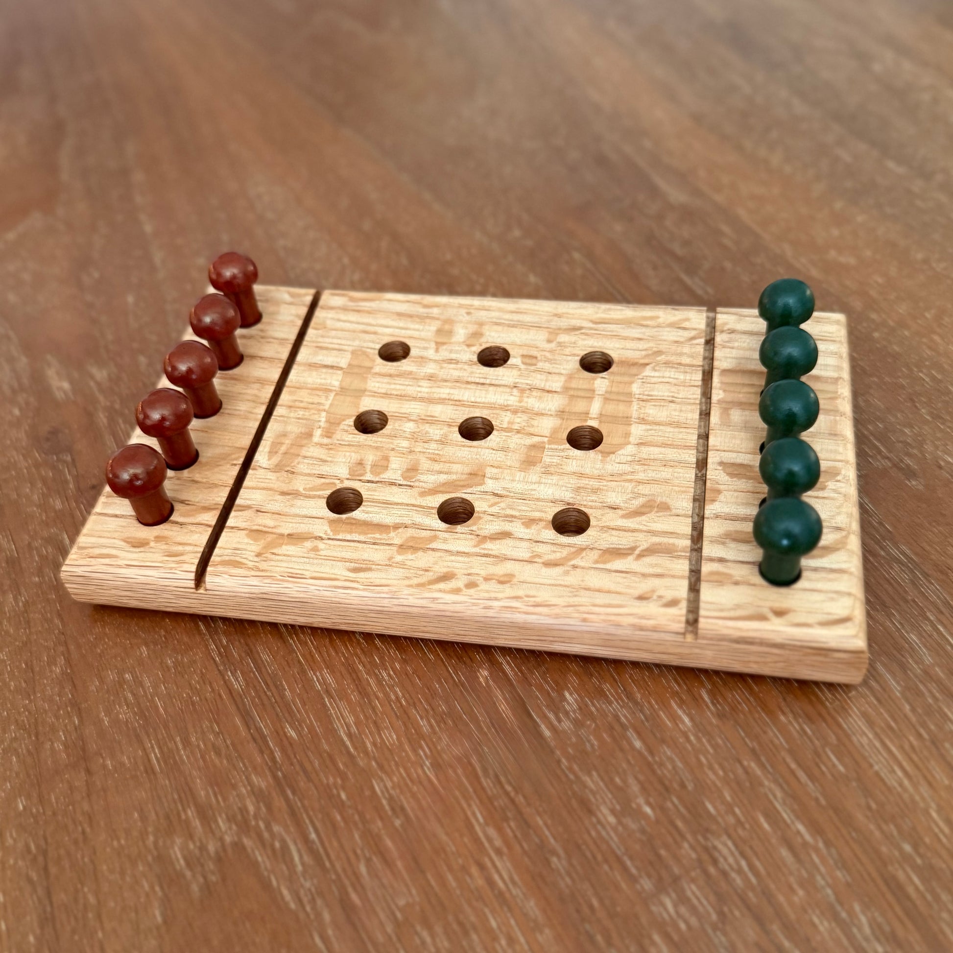 A small wooden tic-tac-toe game board  sitting on a table with rust colored playing pegs and dark green colored playing pegs.