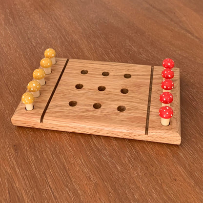Wooden red oak tic tac toe board game with yellow and red mushroom playing pegs on a wooden surface