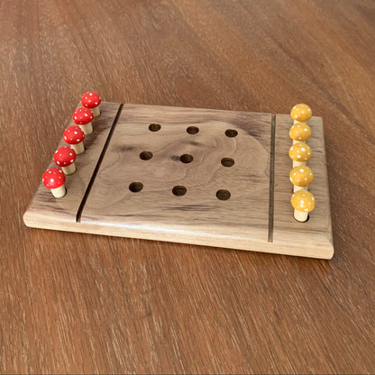 Walnut wooden tic tac toe board game with red and yellow mushroom pegs on a wooden surface
