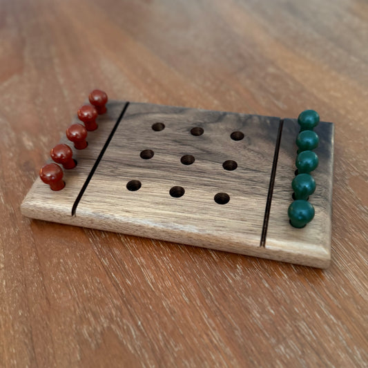 a wooden tic-tac-toe game board with rust and green colored playing pegs, sitting on a wooden table.