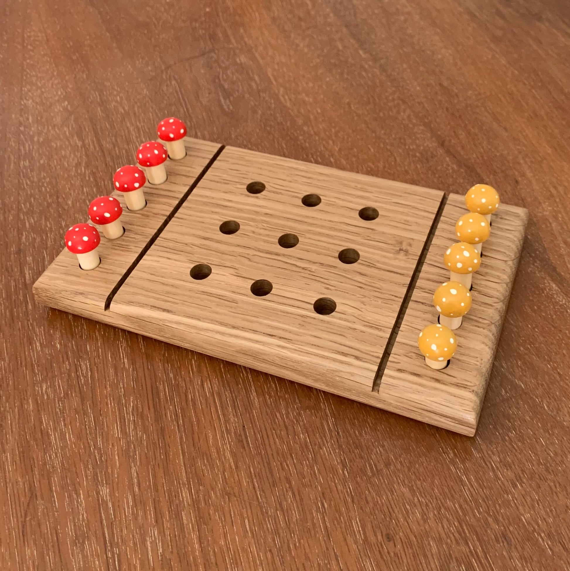 White Oak wooden tic tac toe board game with yellow and red mushroom playing pegs on a wooden surface