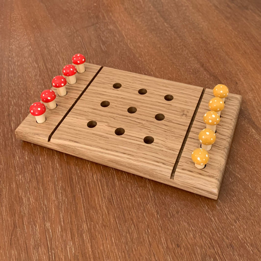 White Oak wooden tic tac toe board game with yellow and red mushroom playing pegs on a wooden surface