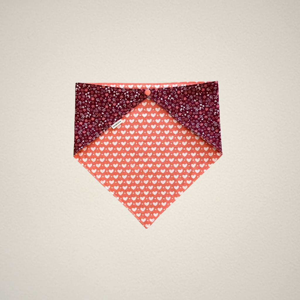 Extra large pet bandana with a pink heart pattern fabric on one side and a dark red floral pattern on the other side, on a beige background.